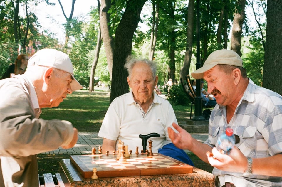 Three older men playing chess together in a park.